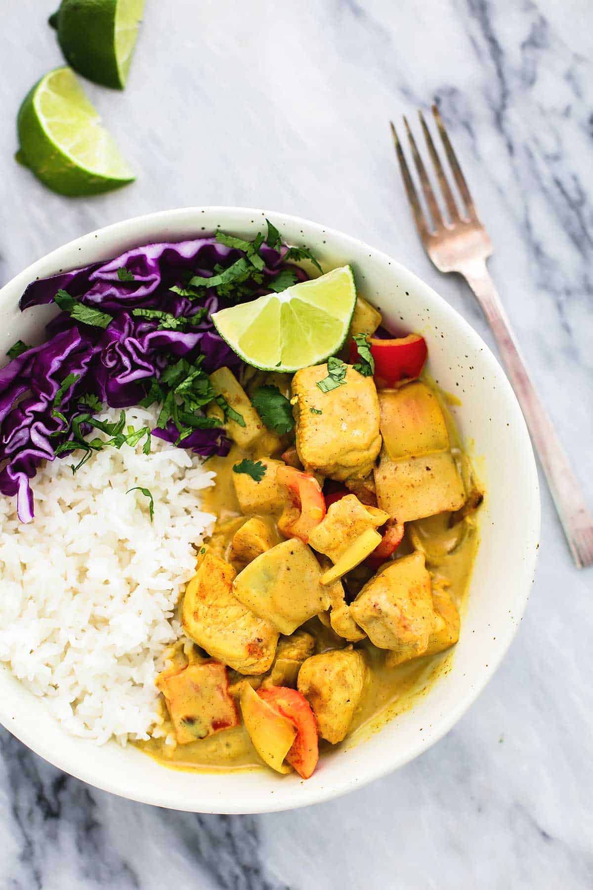 top view of coconut curry chicken with rice in a bowl with lime slices and a fork on the side.