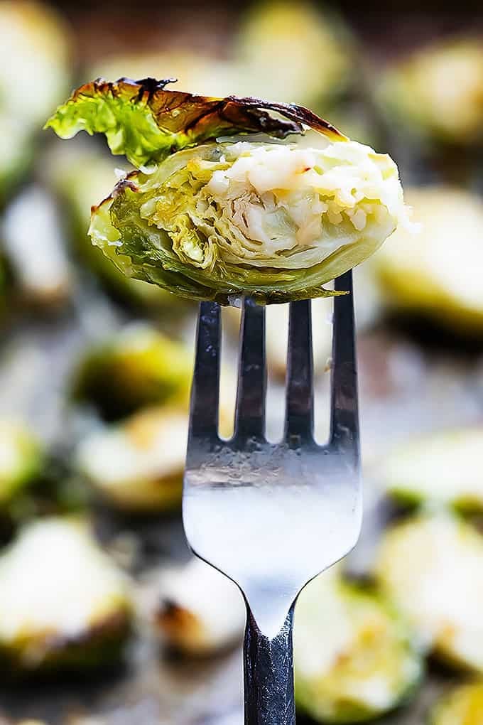a roasted garlic parmesan brussel sprout on a fork with more brussel sprouts faded in the background.