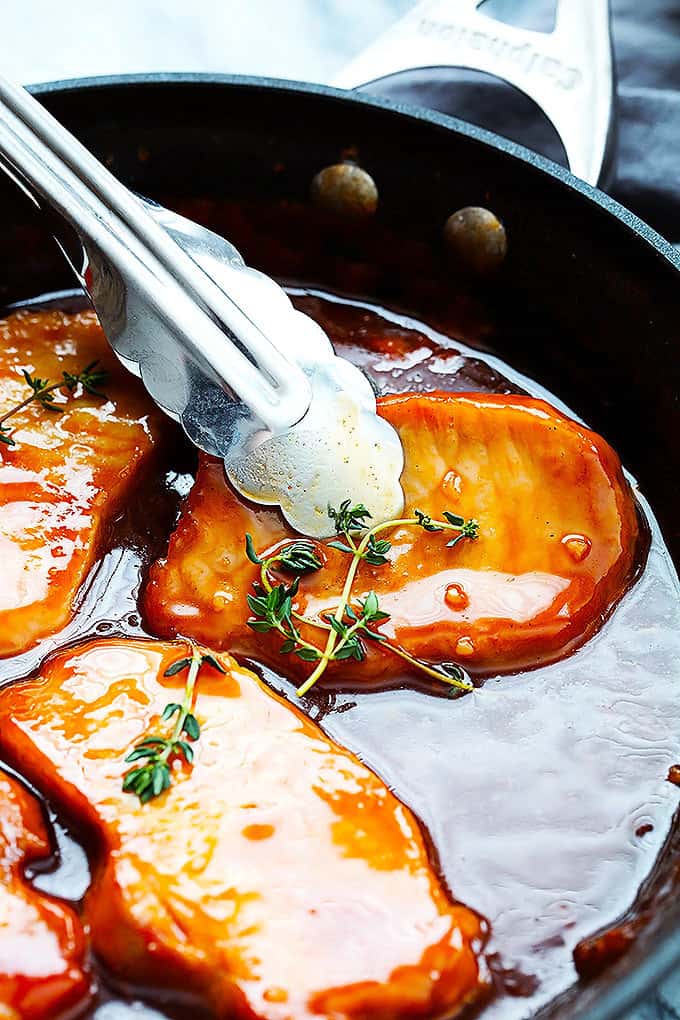 tongs picking up a maple glazed porkchop with more porkchops around it in a skillet.