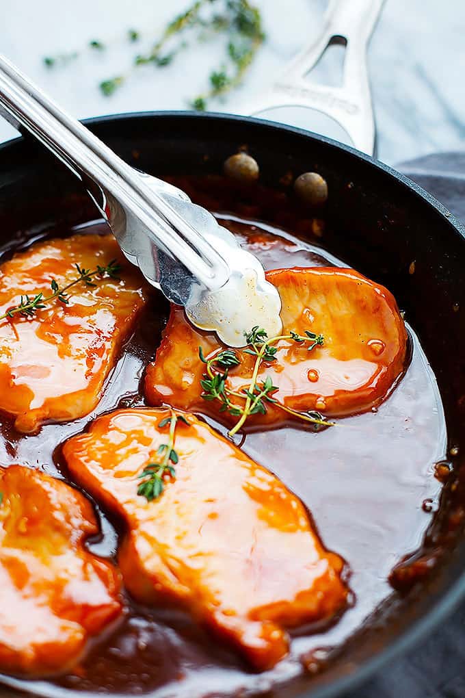 tongs picking up a maple glazed porkchop with more porkchops around it in a skillet.