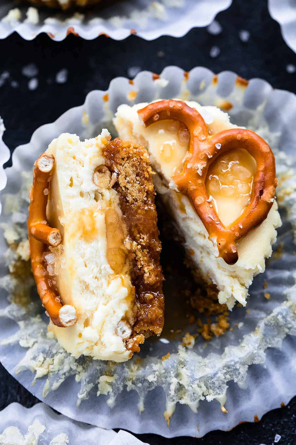 close up of a salted caramel pretzel mini cheesecake cut in half with the liner opened.