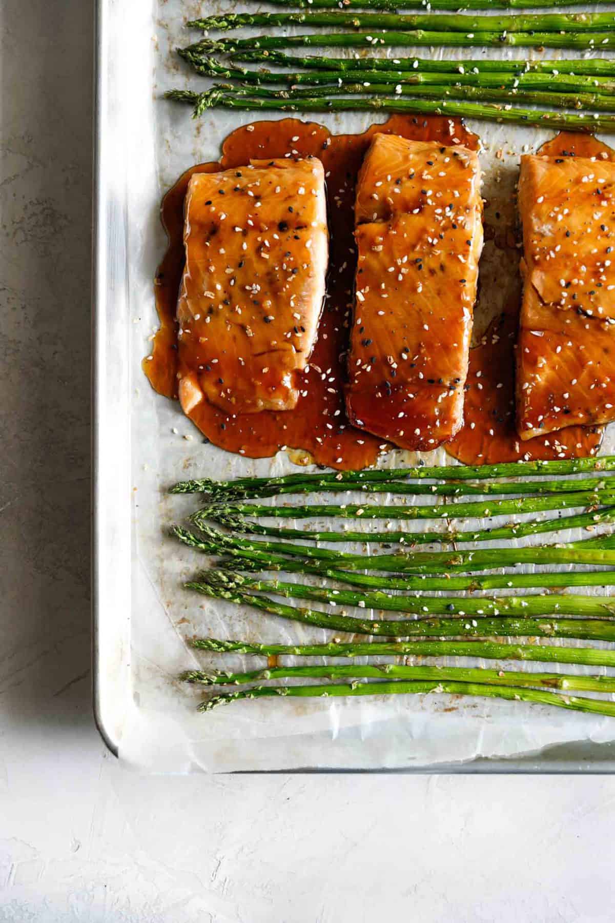 close up top view of baked sesame glazed salmon and asparagus on a baking sheet.