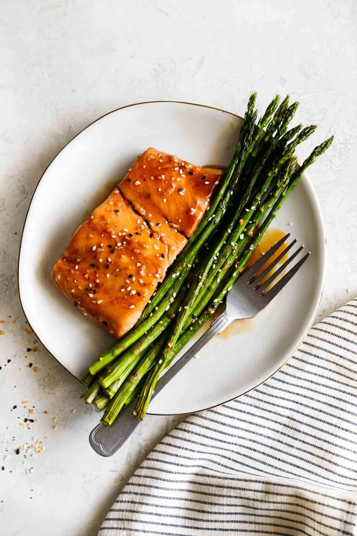 top view of baked sesame glazed salmon and asparagus with a fork on a plate.