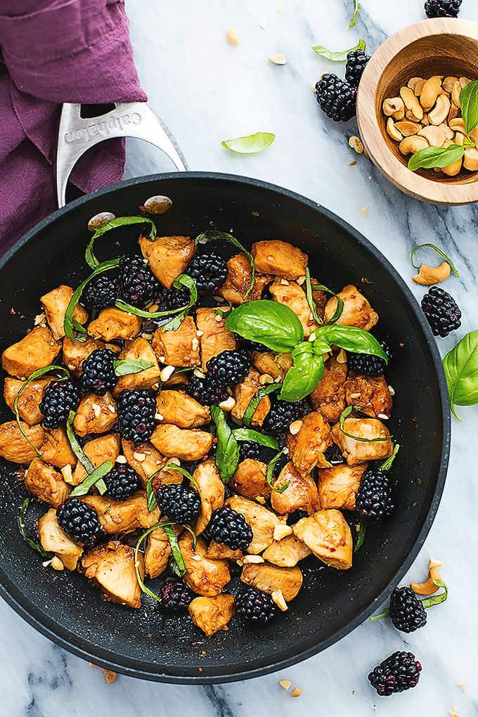 top view of Thai blackberry basil chicken in a skillet with cashews and blackberries on the side.