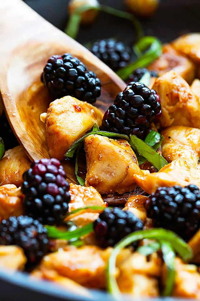close up of Thai blackberry basil chicken and a wooden serving spoon.