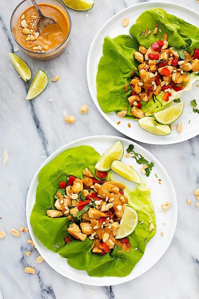 top view of Thai peanut chicken lettuce wraps with lime slices and a glass of peanut sauce with a spoon in it on the side.