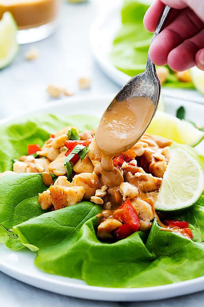 a hand putting peanut sauce on a Thai peanut chicken lettuce wrap with a spoon.