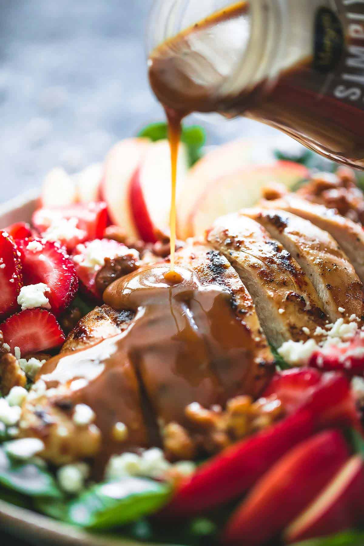 close up of creamy balsamic dressing being poured on top of balsamic chicken, strawberry, and apple salad.