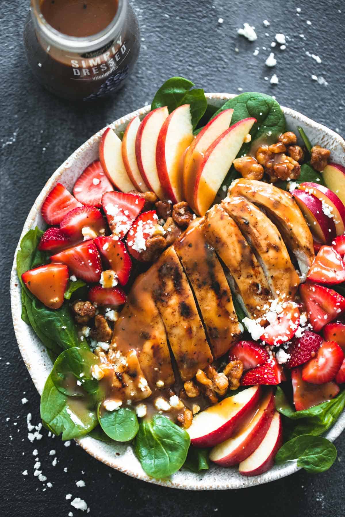 top view of balsamic chicken, strawberry, and apple salad on a plate with balsamic dressing in a jar on the side.