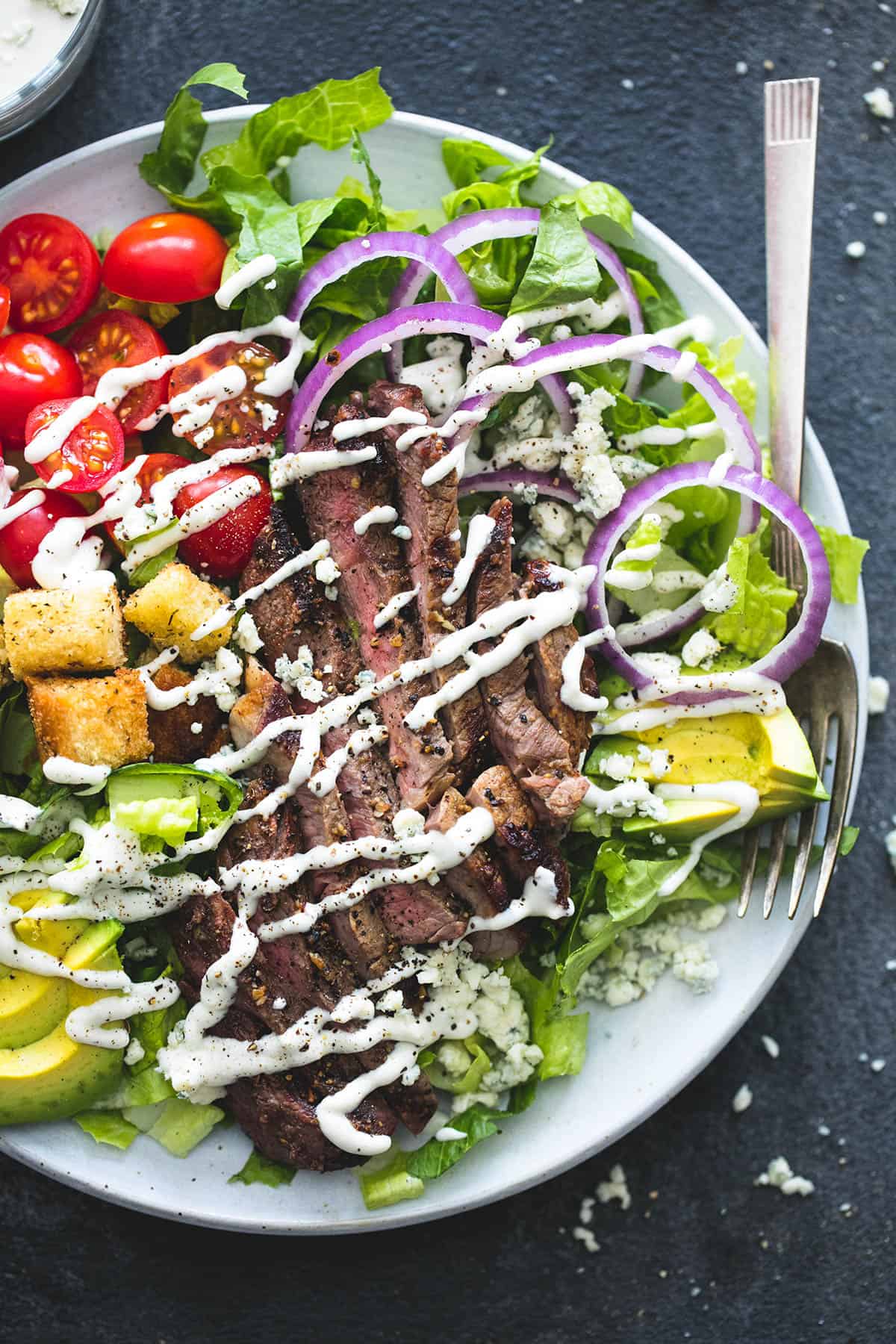 top view of black n' blue grilled steak salad and a fork on a plate.