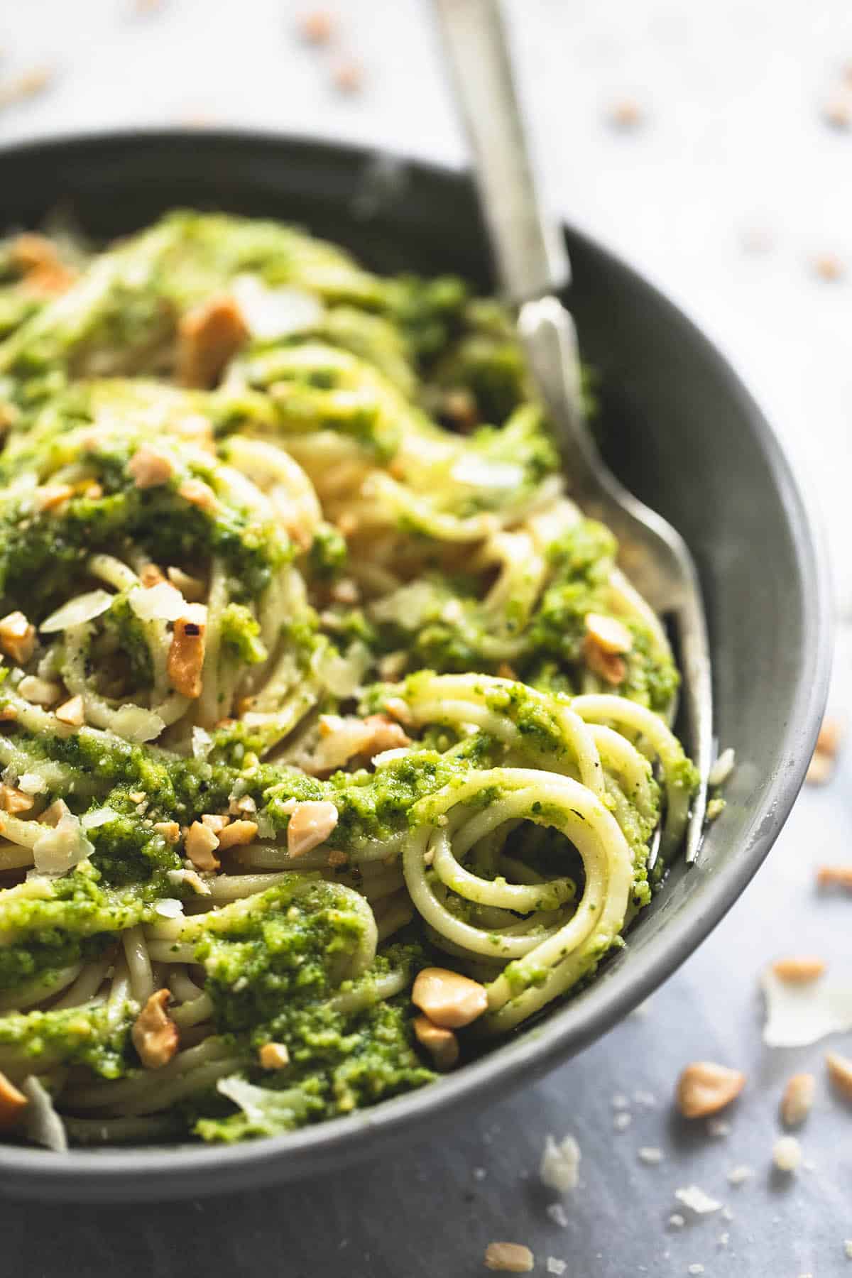 close up of cashew pesto pasta with a fork in a bowl surrounded by crushed cashews.