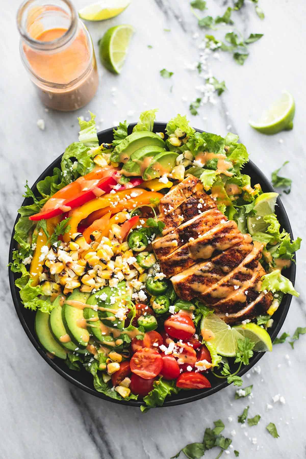 top view of fiesta lime chicken salad with chipotle dressing in a bowl with more dressing in a jar and lime slices on the side.