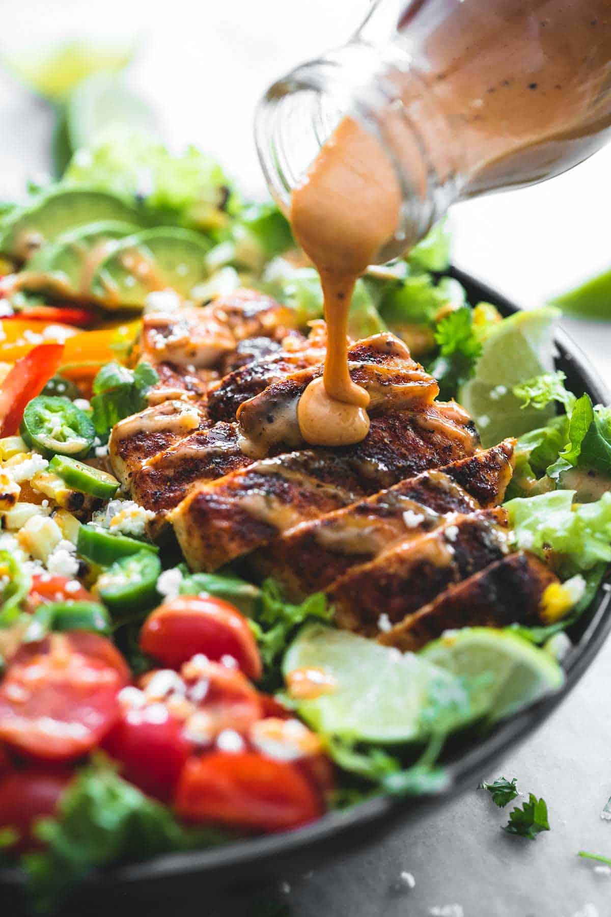 close up of fiesta lime chicken salad with chipotle dressing in a bowl with chipotle dressing being poured on top.