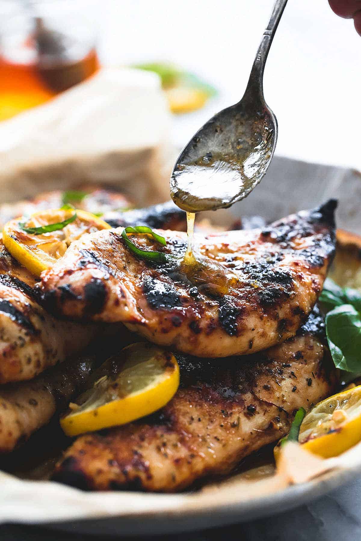 a hand pouring sauce on top of grilled honey lemon chicken on a plate.