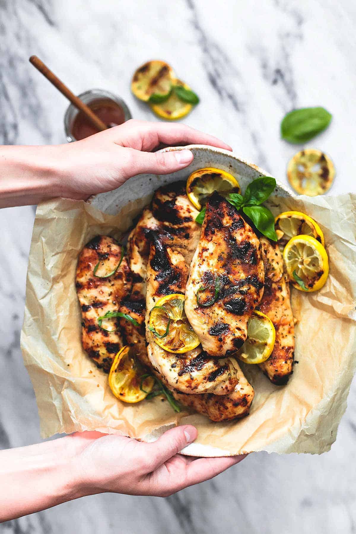 top view of hands holding up a plate of grilled honey lemon chicken.