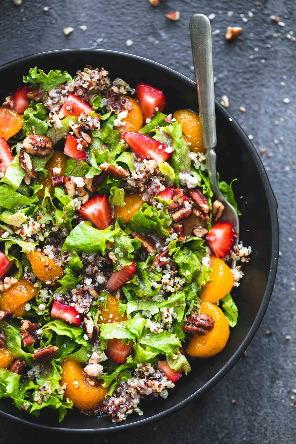 top view of mandarin strawberry quinoa chopped salad and a fork in a bowl.