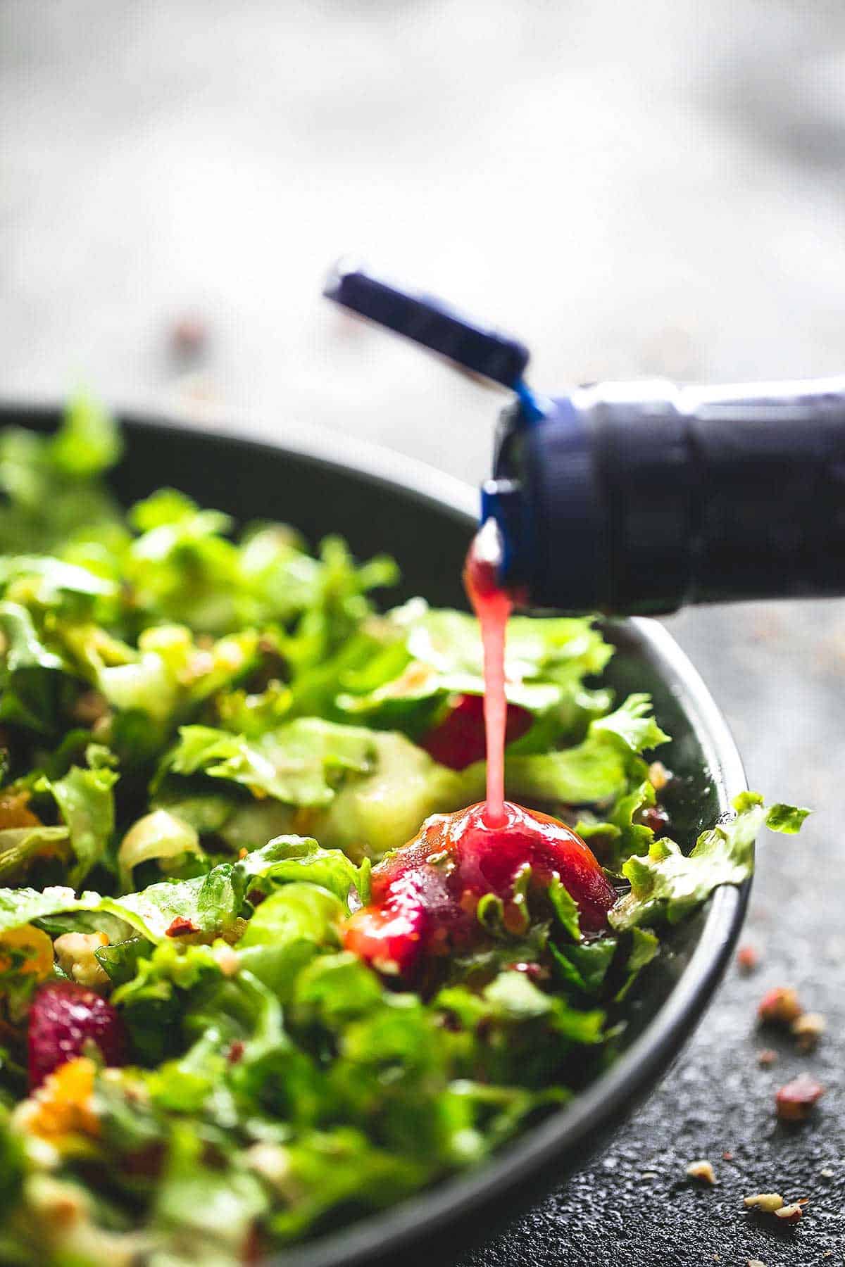 berry vinaigrette being poured on top of mandarin strawberry quinoa chopped salad in a bowl.  