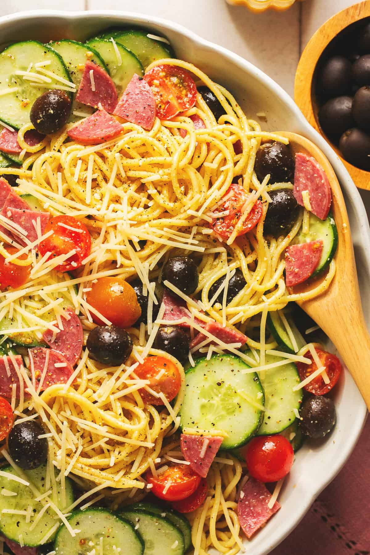 Overhead close up of Italian spaghetti pasta salad with creamy dressing and a wooden serving spoon in a white bowl.