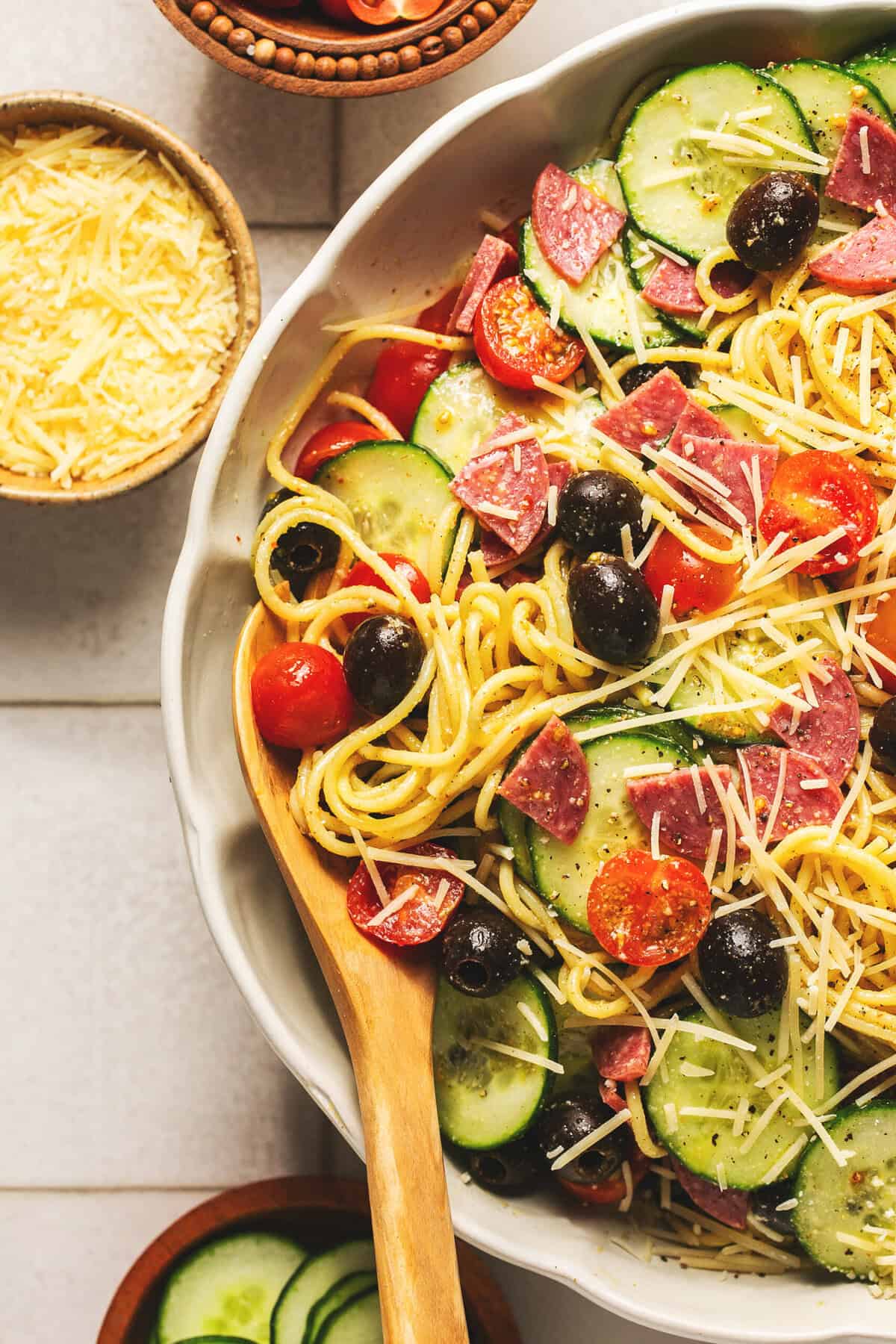 Overhead close up of Italian spaghetti pasta salad with creamy dressing and a wooden serving spoon in a white bowl.