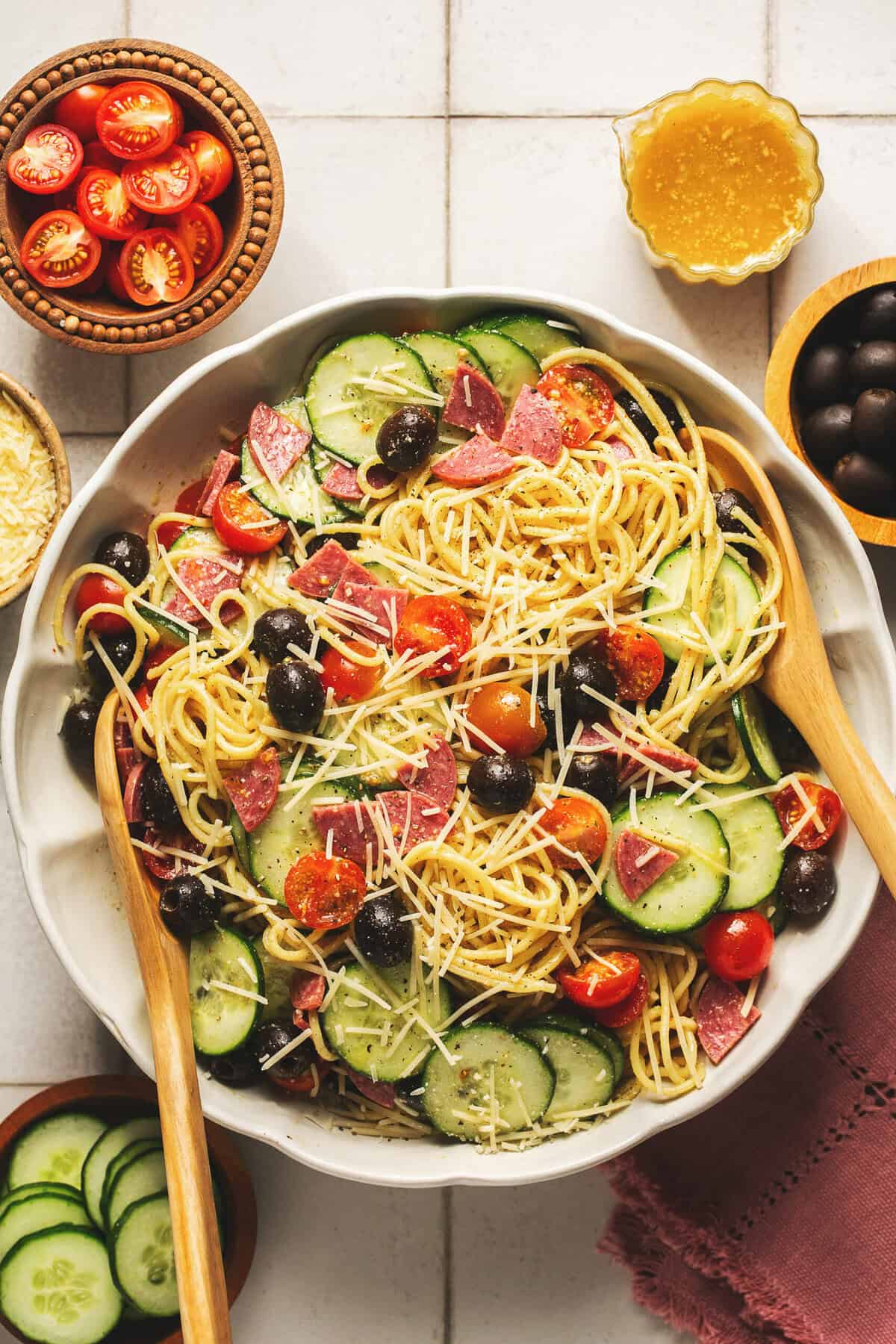 Overhead of Italian spaghetti pasta salad with creamy dressing with wooden serving spoons in a white bowl.