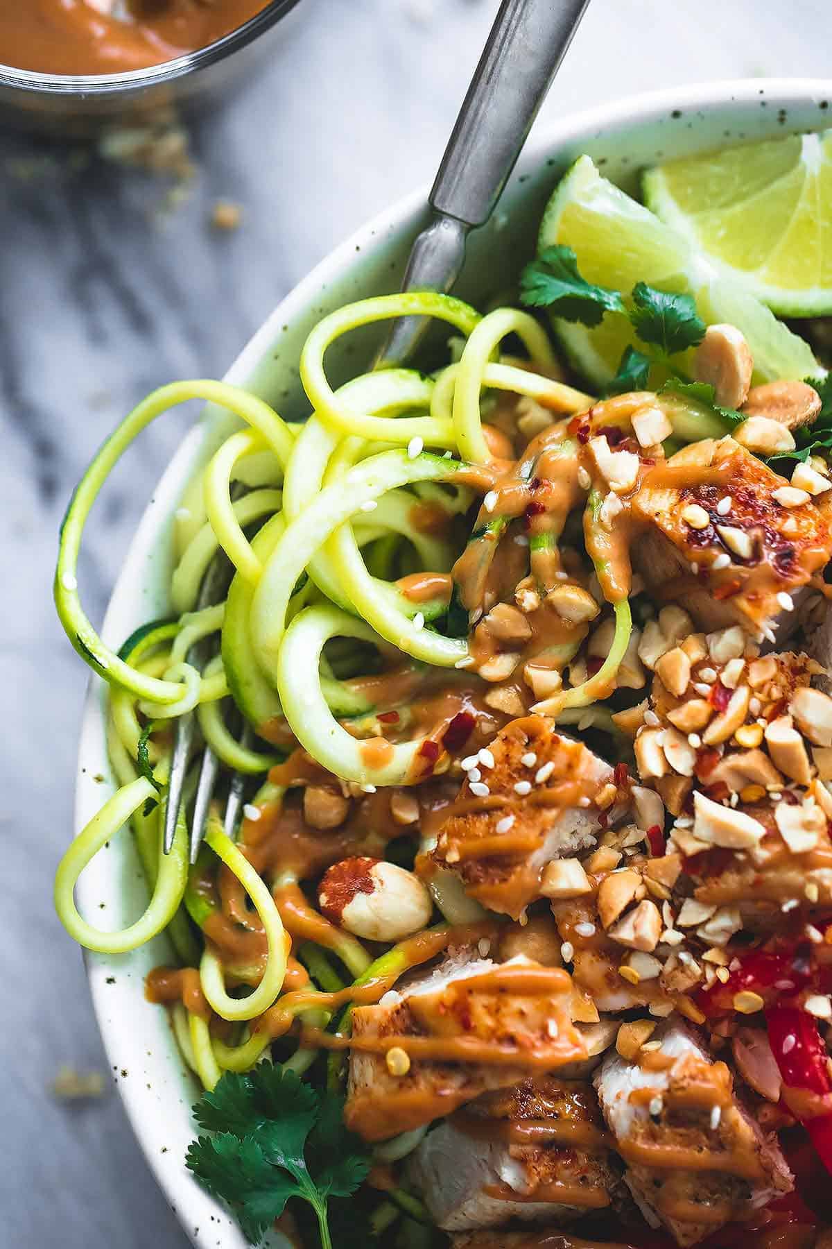 close up of a Thai peanut chicken & zucchini noodle bowl with a fork.