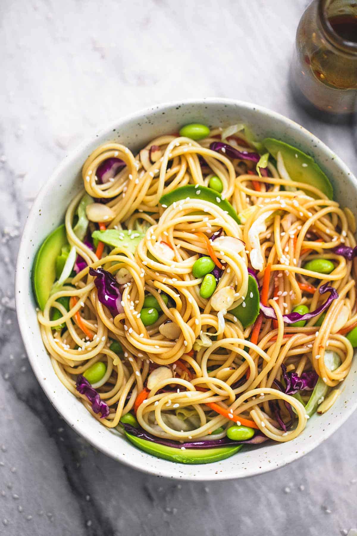 close up of Asian spaghetti salad with sesame ginger dressing in a bowl with a jar of more dressing on the side.