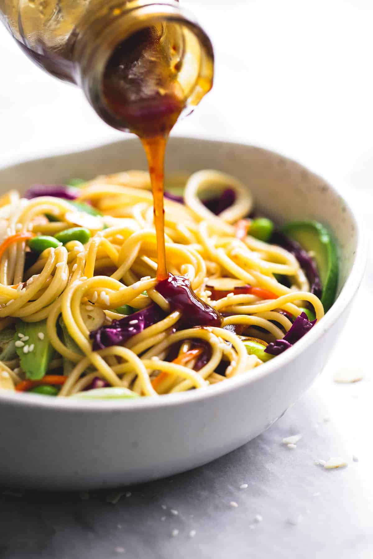 sesame ginger dressing being poured on top of Asian spaghetti salad in a bowl.