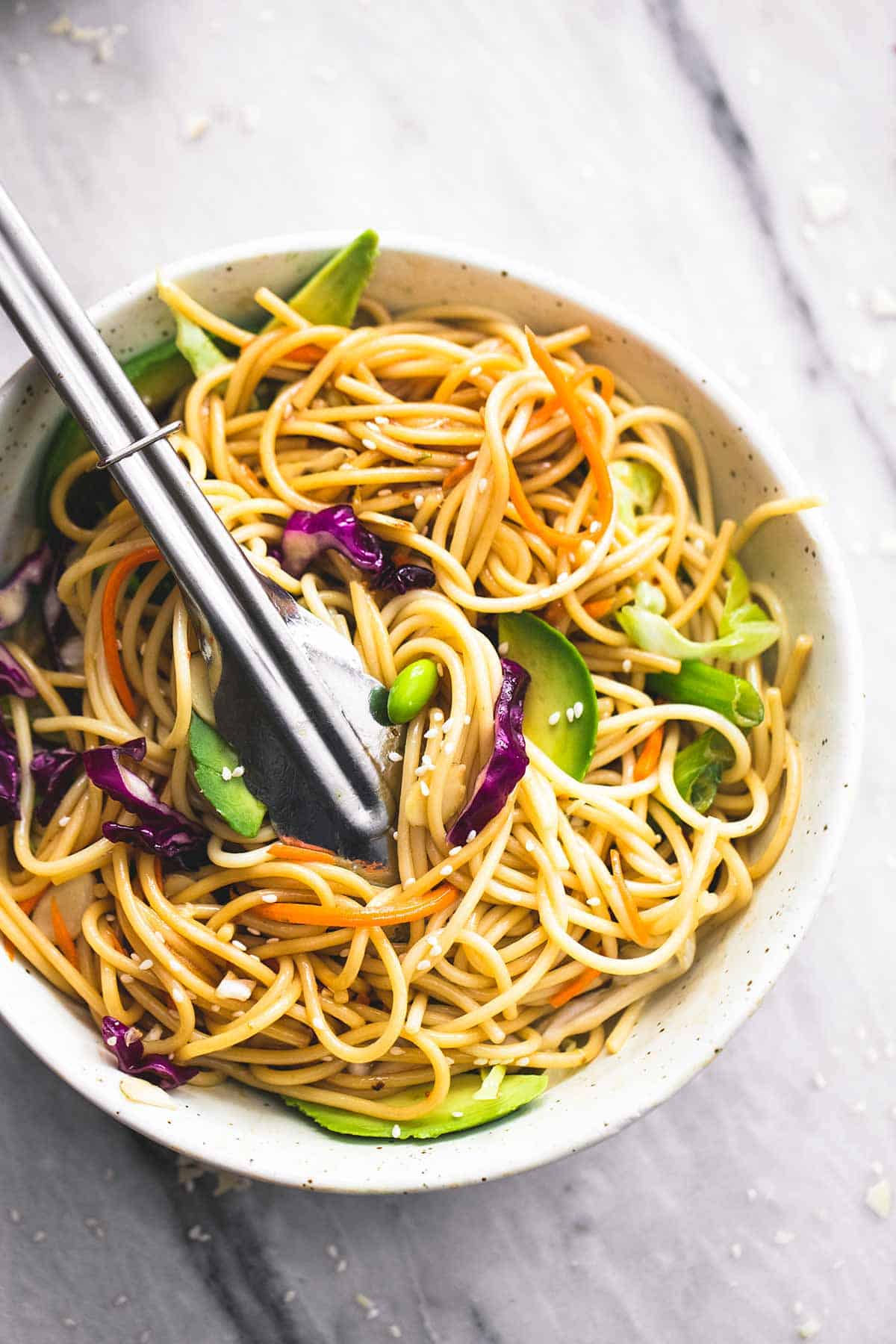 top view of Asian spaghetti salad with sesame ginger dressing with tongs in a bowl.