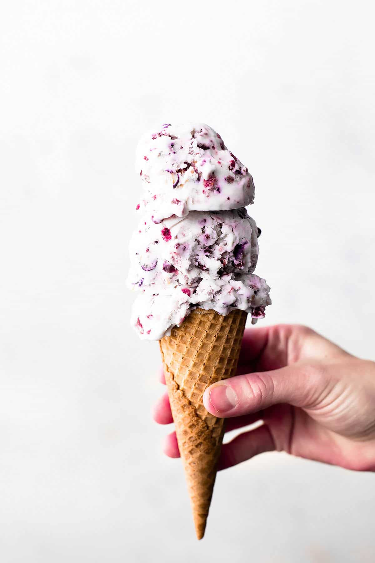 a hand holding an ice cream cone with two scoops of mixed berry ice cream.