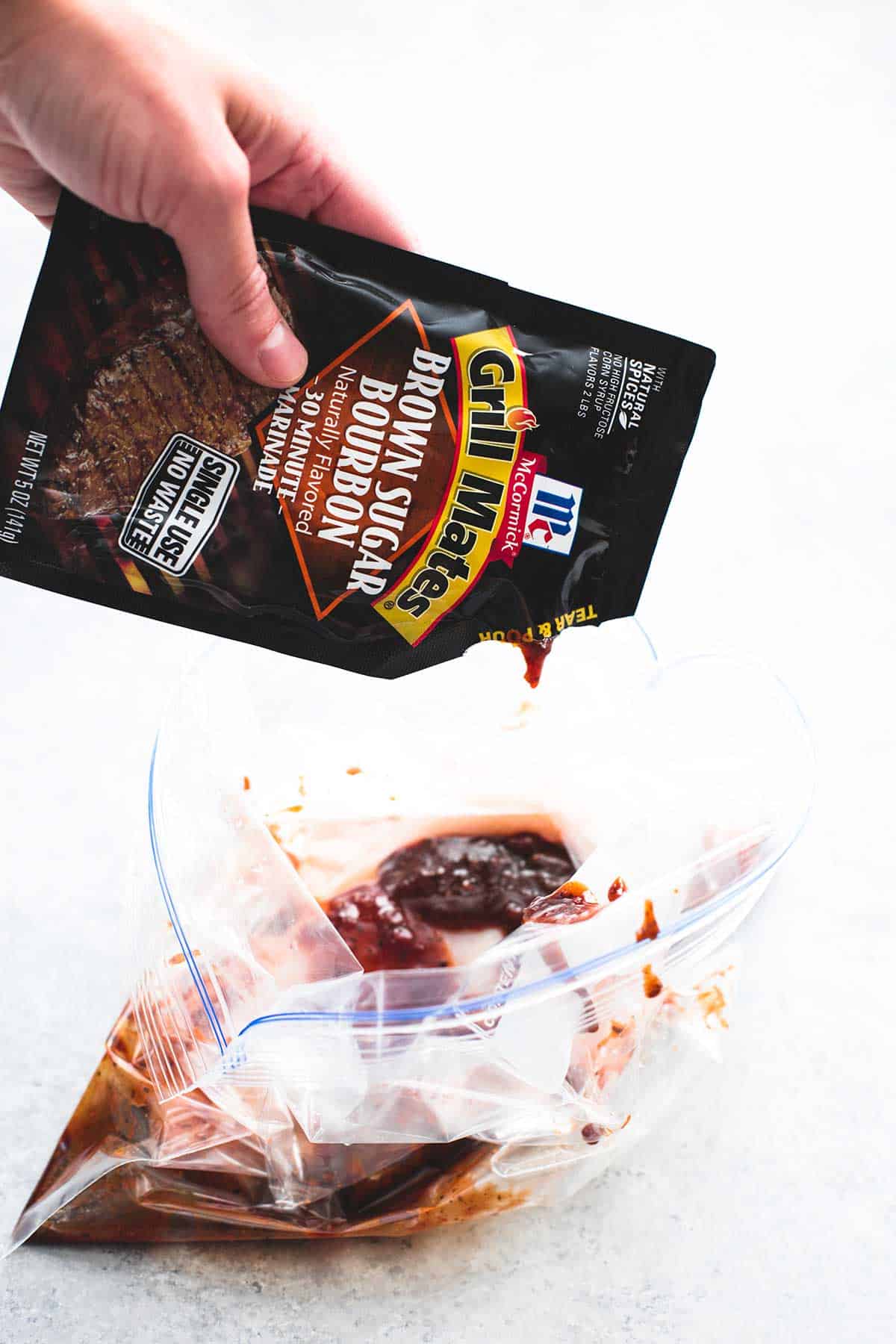 a hand pouring a brown sugar bourbon marinade package in a zip lock bag.