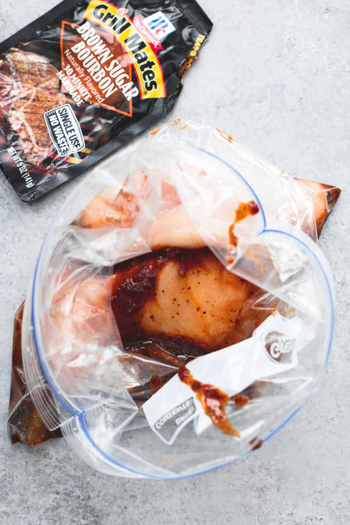 top view of chicken with brown sugar bourbon marinade in a zip lock bag with the marinade package on the side.