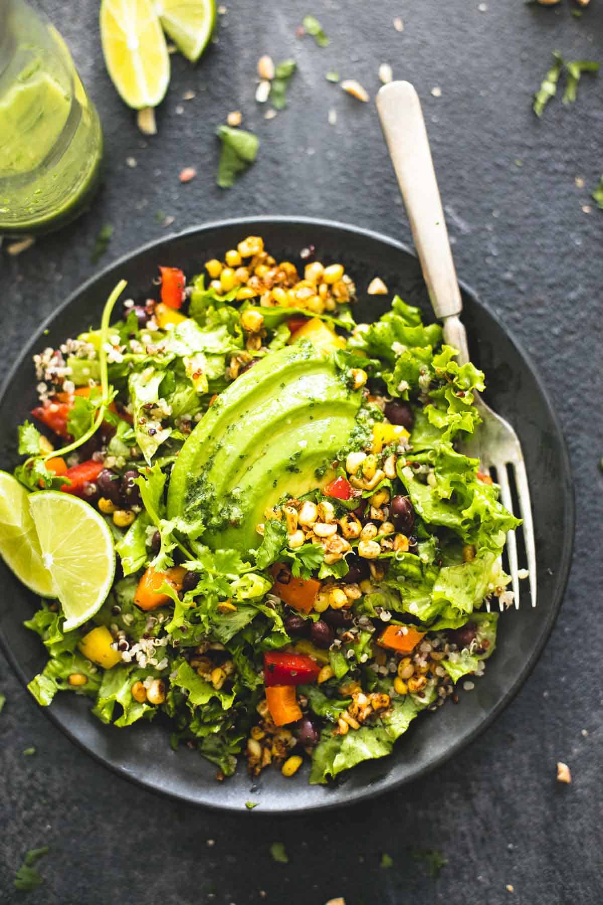 top view of chopped fiesta quinoa salad with cilantro lime dressing with a fork on a plate with lime slices on the side.