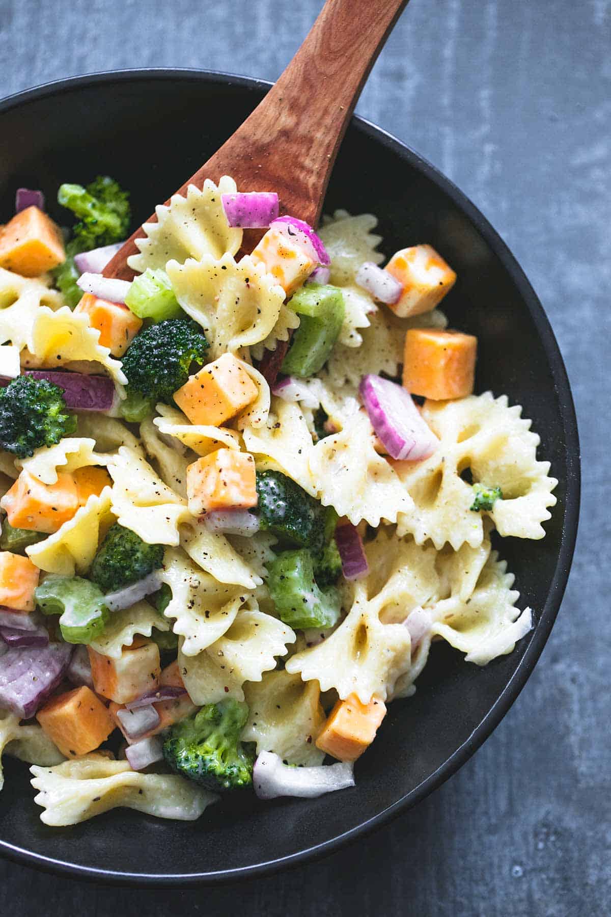 close up top view of creamy cheddar broccoli salad and a wooden serving spoon in a bowl.