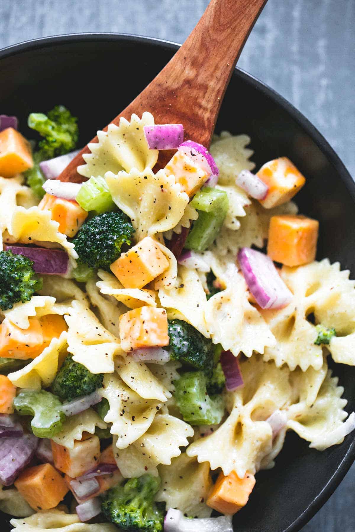 close up top view of creamy cheddar broccoli salad with a wooden serving spoon on a bowl.