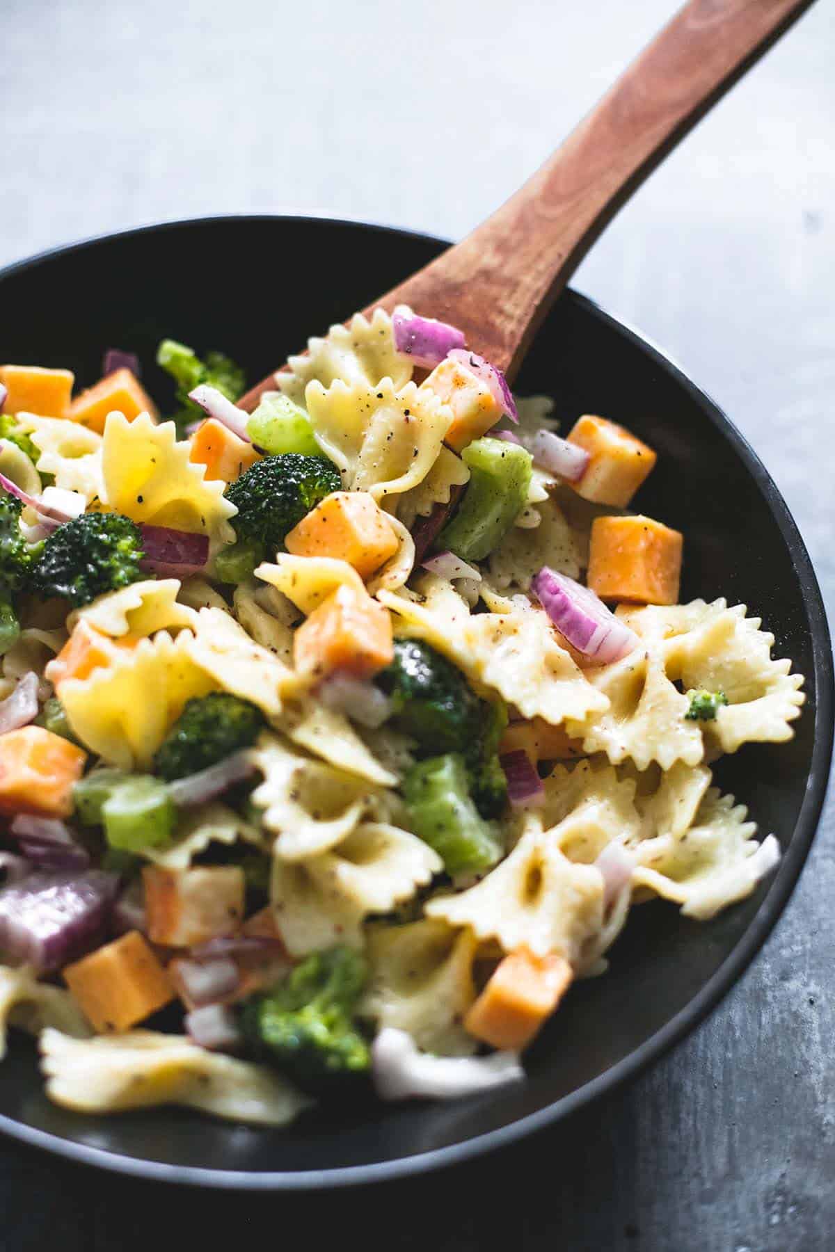 creamy cheddar broccoli salad and a wooden serving spoon in a bowl.