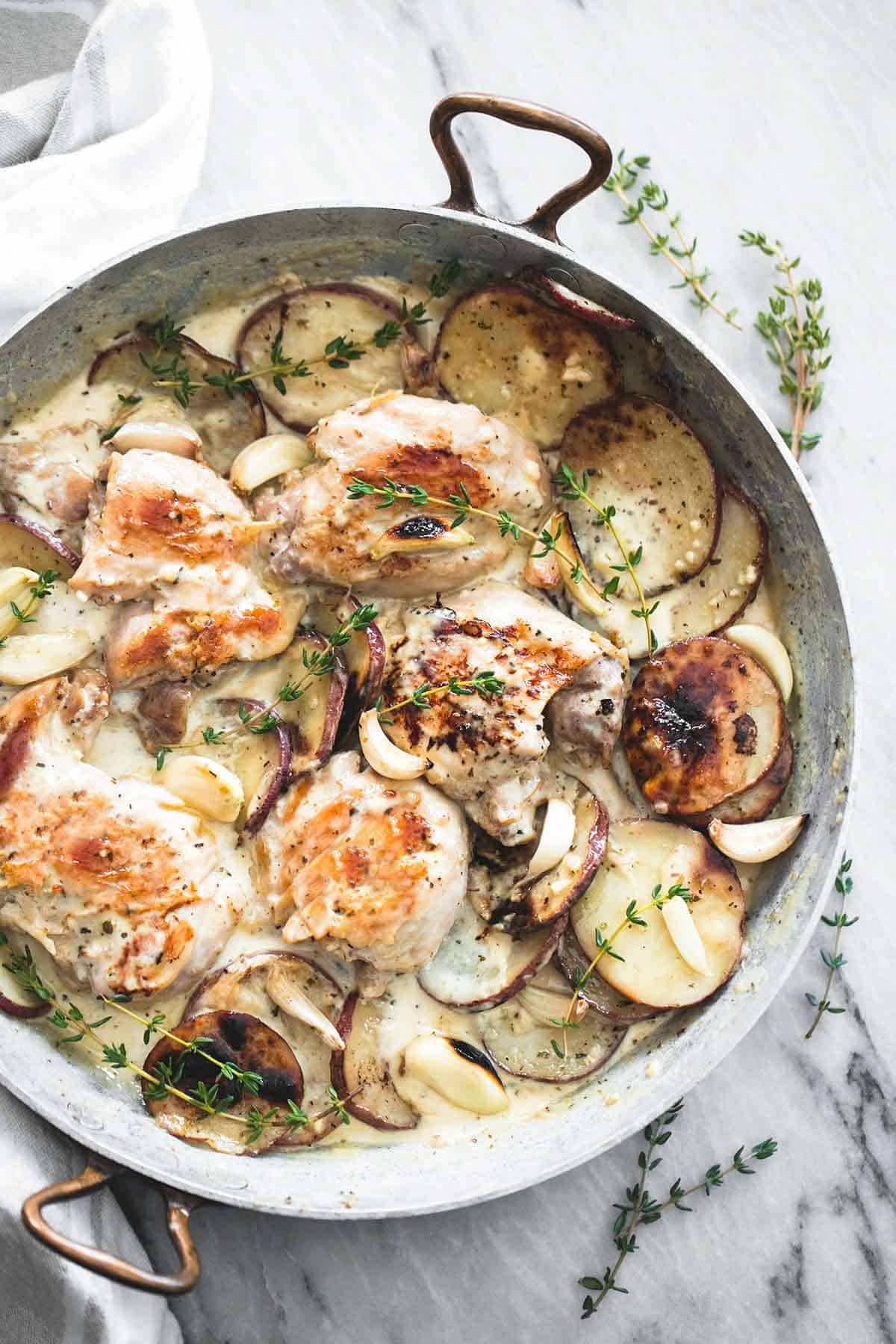 top view of creamy garlic herb chicken & potatoes in a pan.