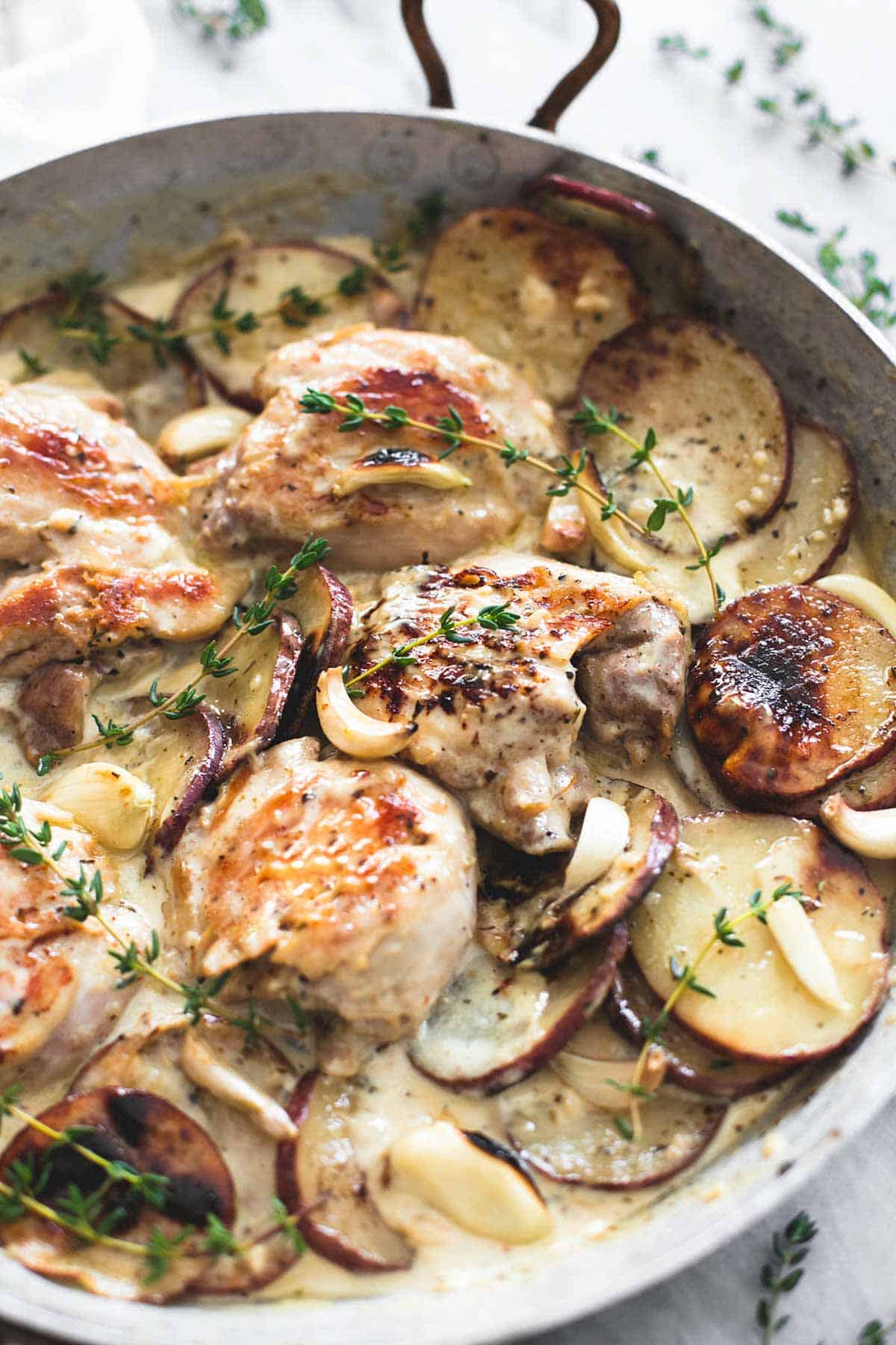 close up of creamy garlic herb chicken & potatoes in a pan.