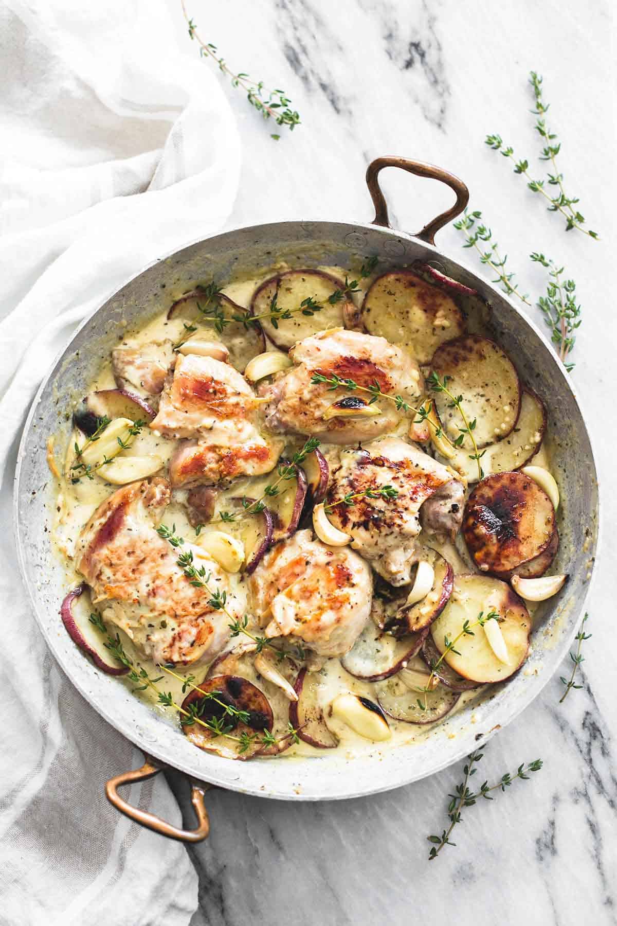 top view of creamy garlic herb chicken & potatoes in a pan.