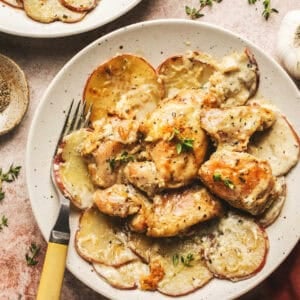 Overhead of oven baked creamy garlic chicken and potatoes and a fork on a white plate.