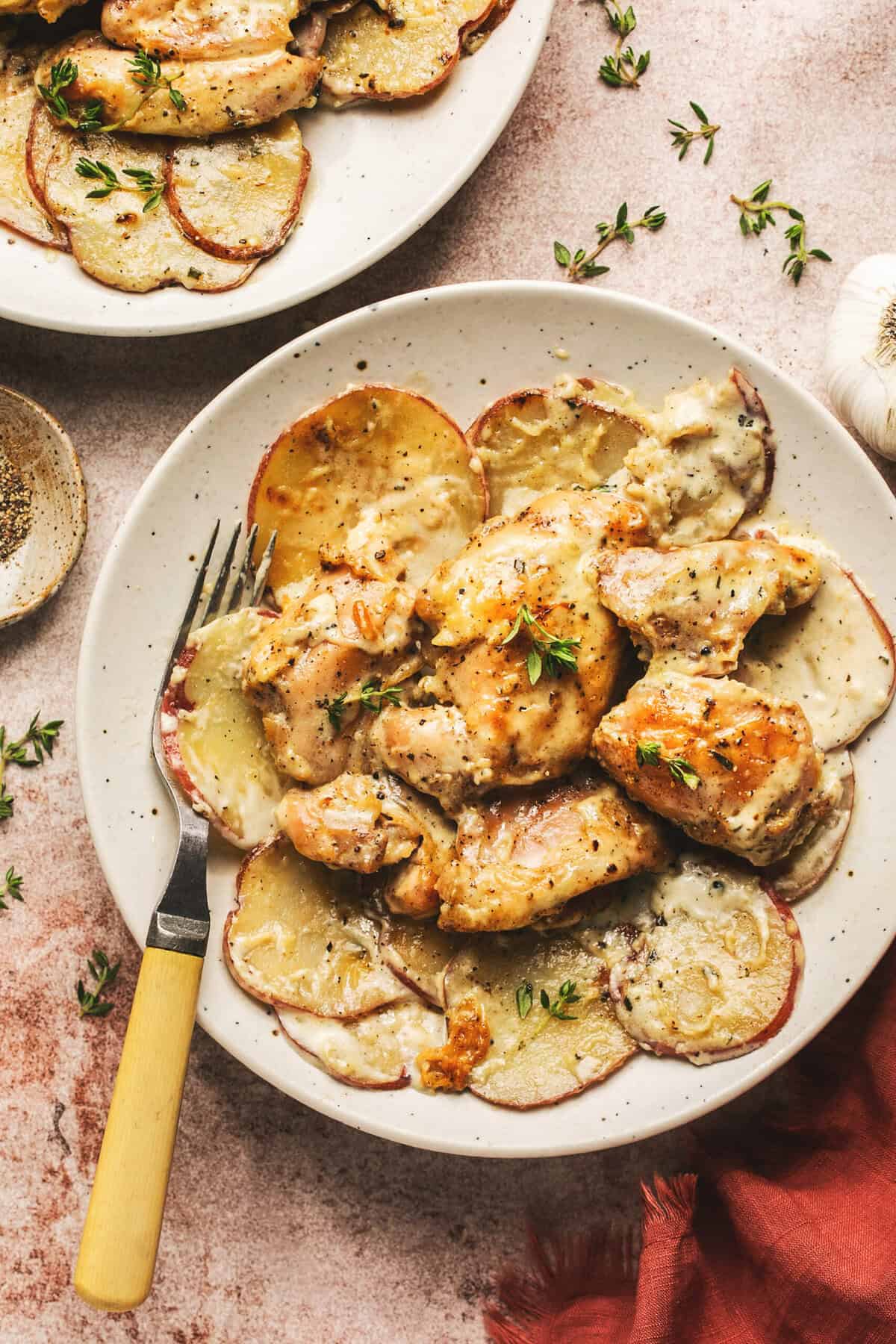 Overhead of oven baked creamy garlic chicken and potatoes and a fork on a white plate.