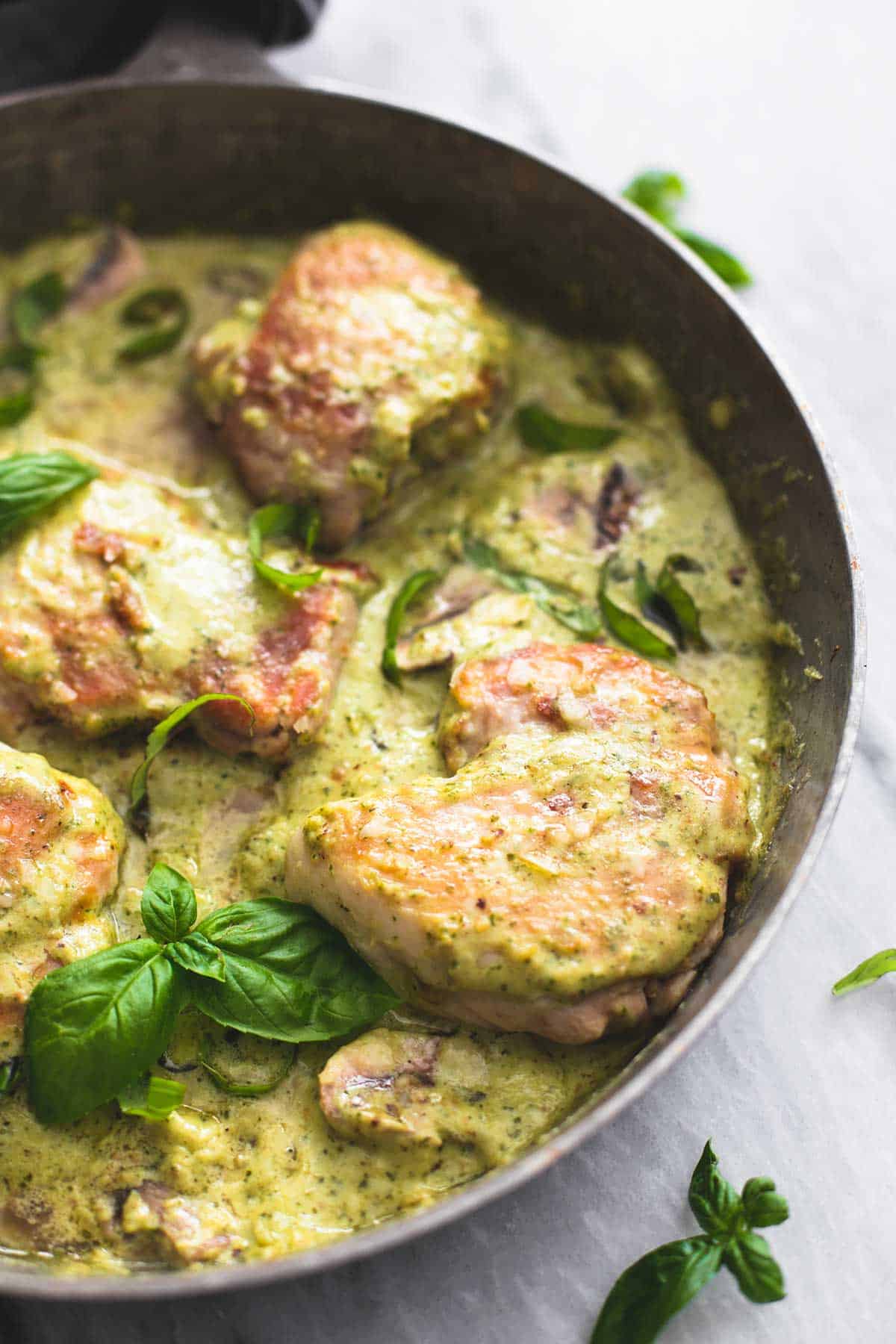 close up of creamy pesto parmesan chicken in a pan.