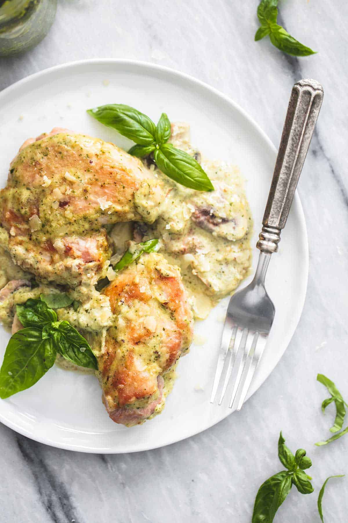 top view of a piece of creamy pesto parmesan chicken and a fork on a plate.