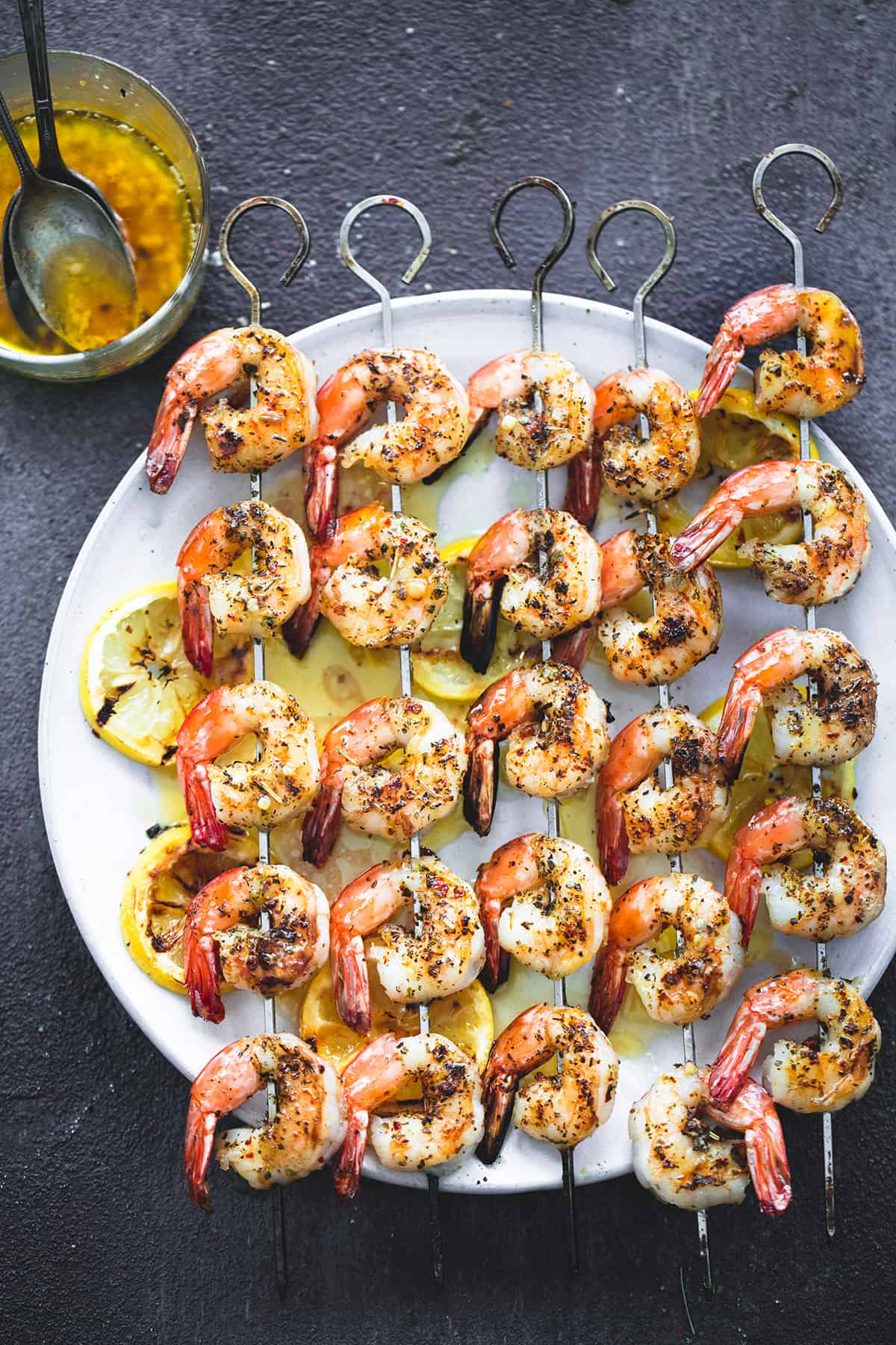 top view of grilled lemon garlic shrimp on skewers with lemon butter mixture and a spoon in a glass on the side.