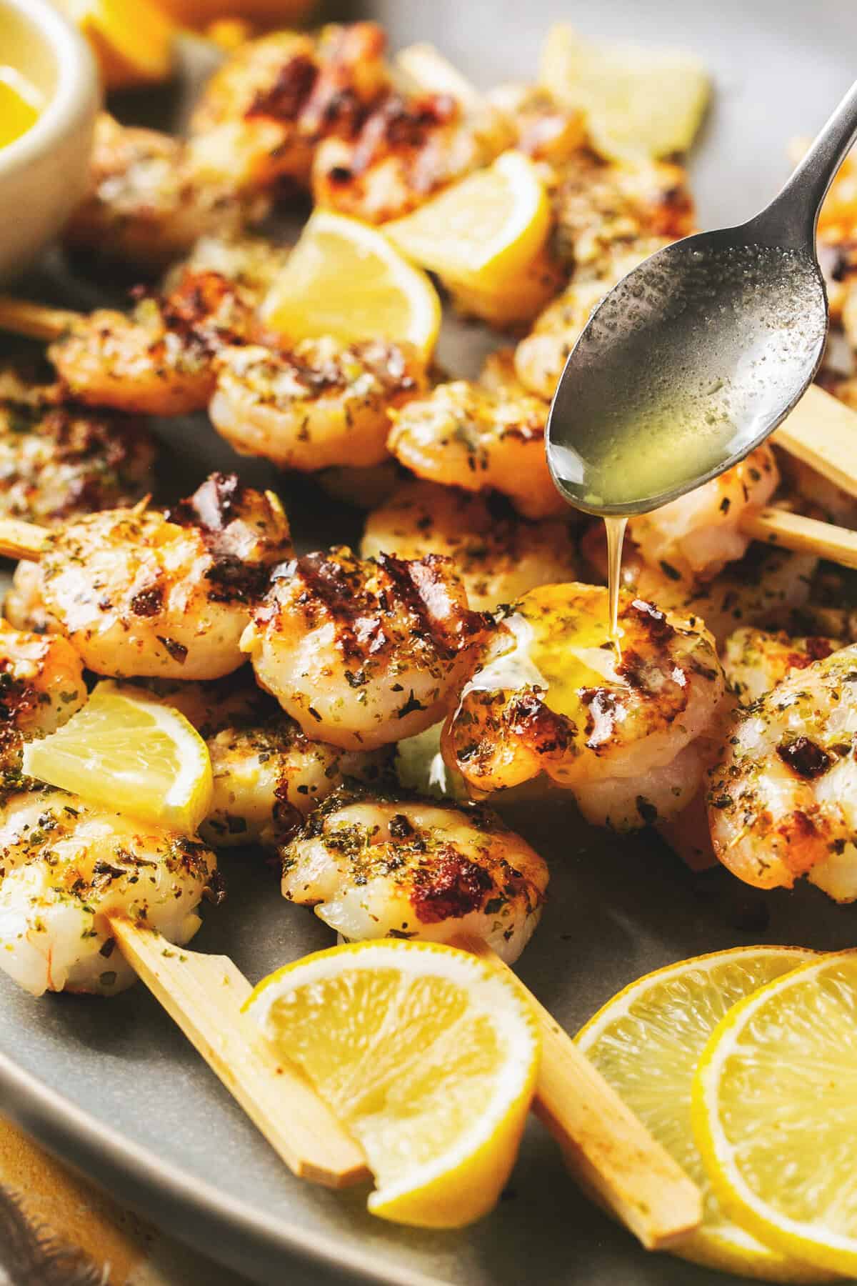 spoon drizzling melted butter onto grilled shrimp.