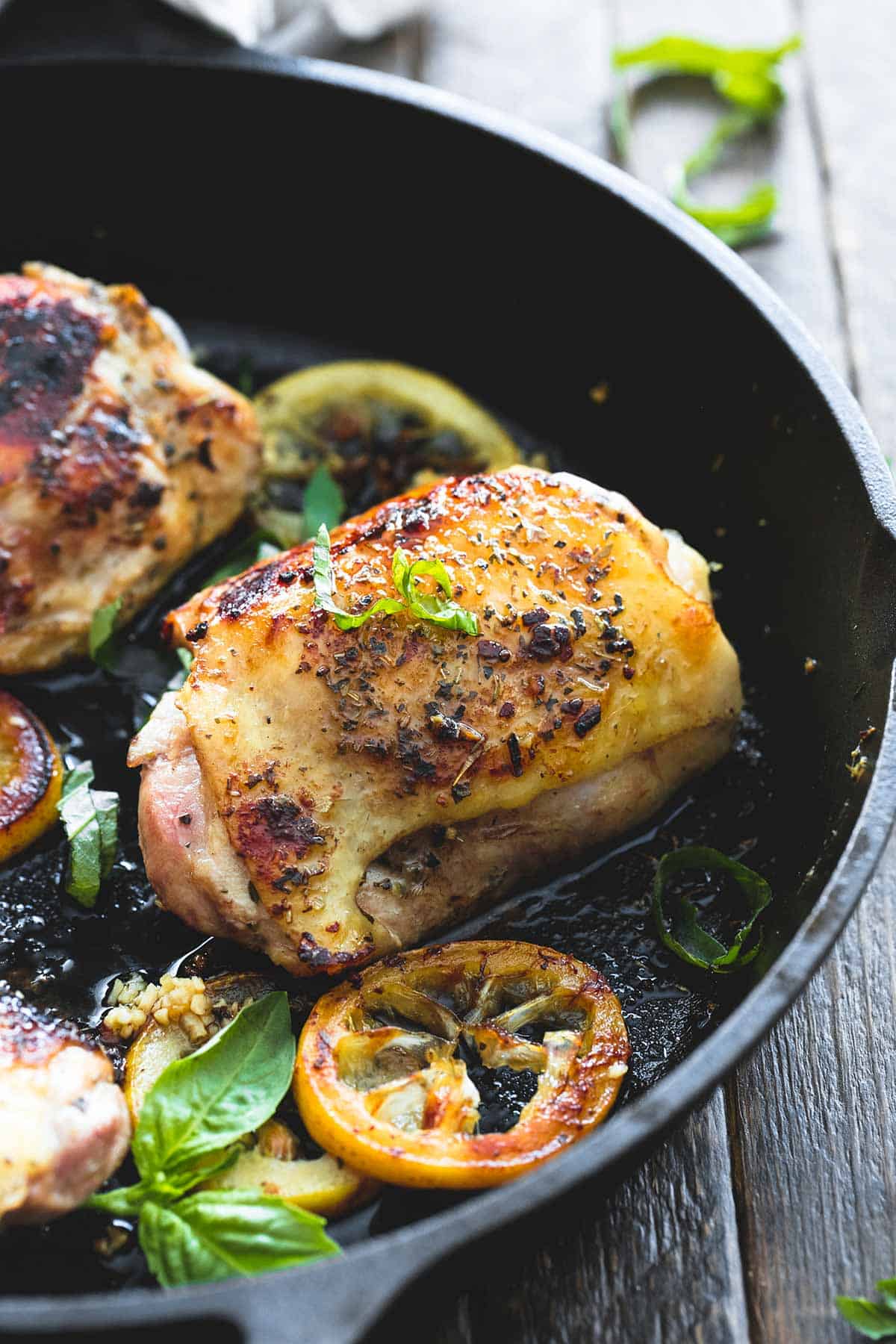 close up of a buttery lemon herb chicken thigh in a skillet with more thighs on the side.