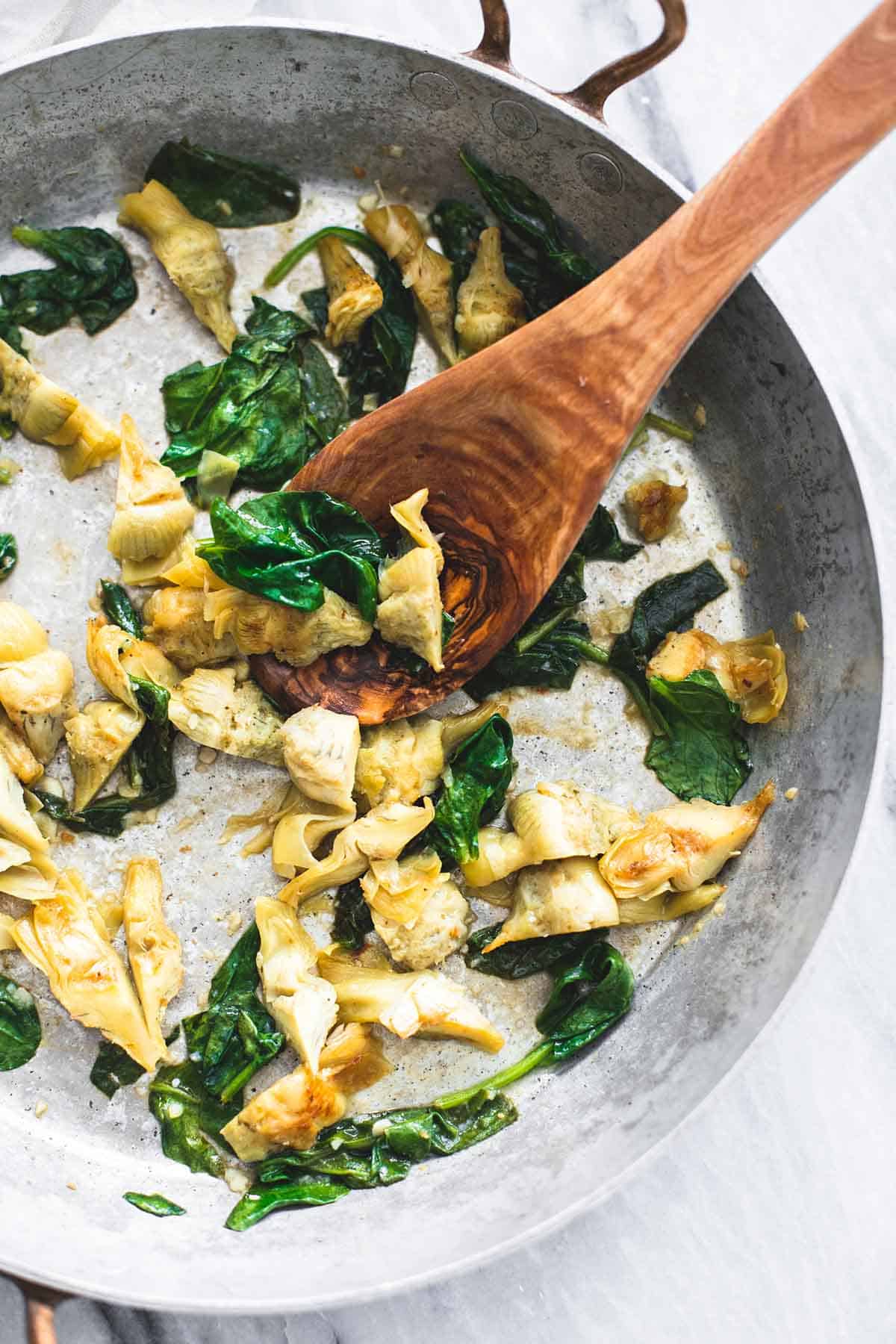 top view of artichoke hearts and spinach with a wooden serving spoon in a skillet.