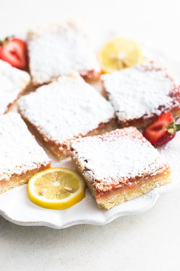 strawberry lemon bars on a plate with lemon wheels and strawberry halves.