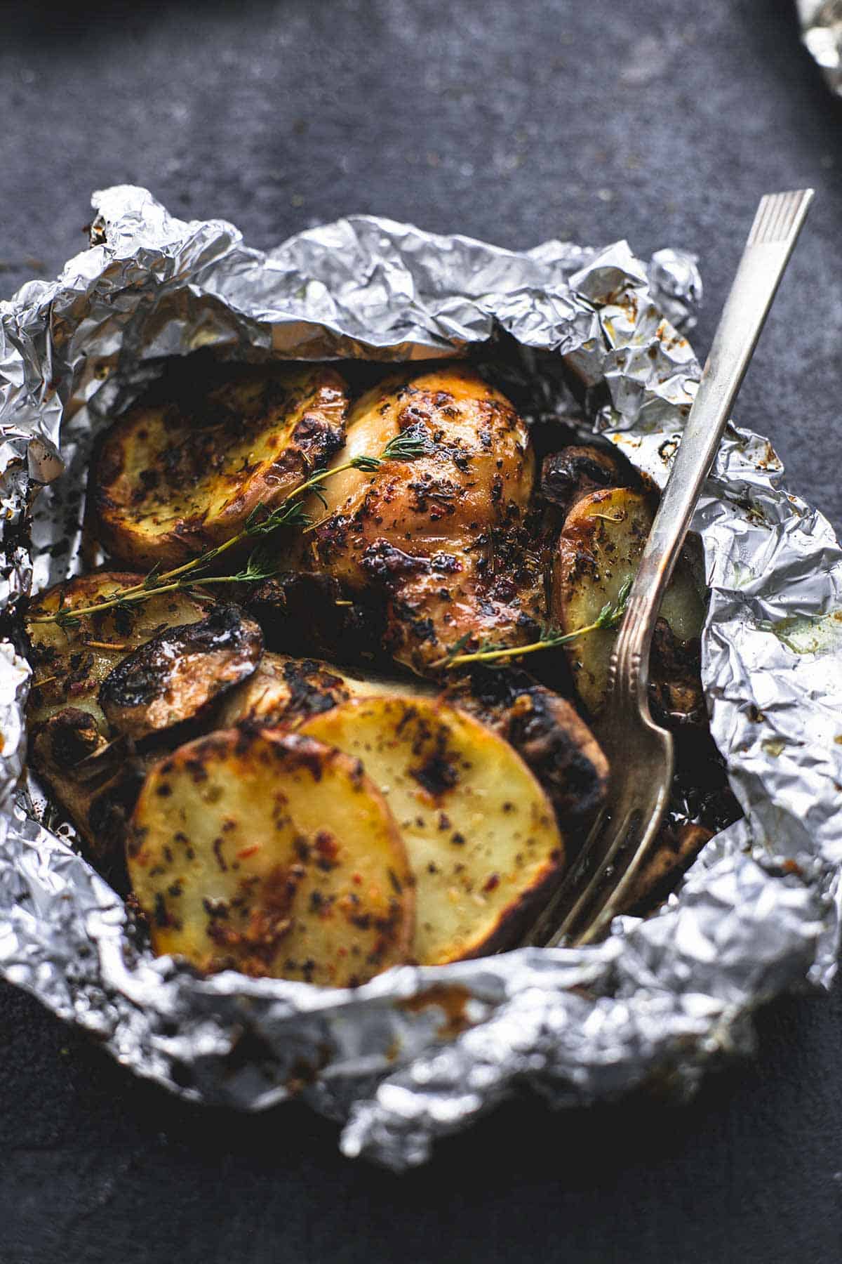 a grilled herbed chicken & potato foil pack with a fork.
