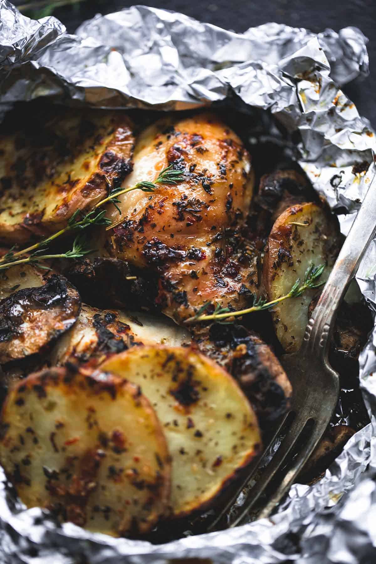 close up of a grilled herbed chicken & potato foil pack with a fork.