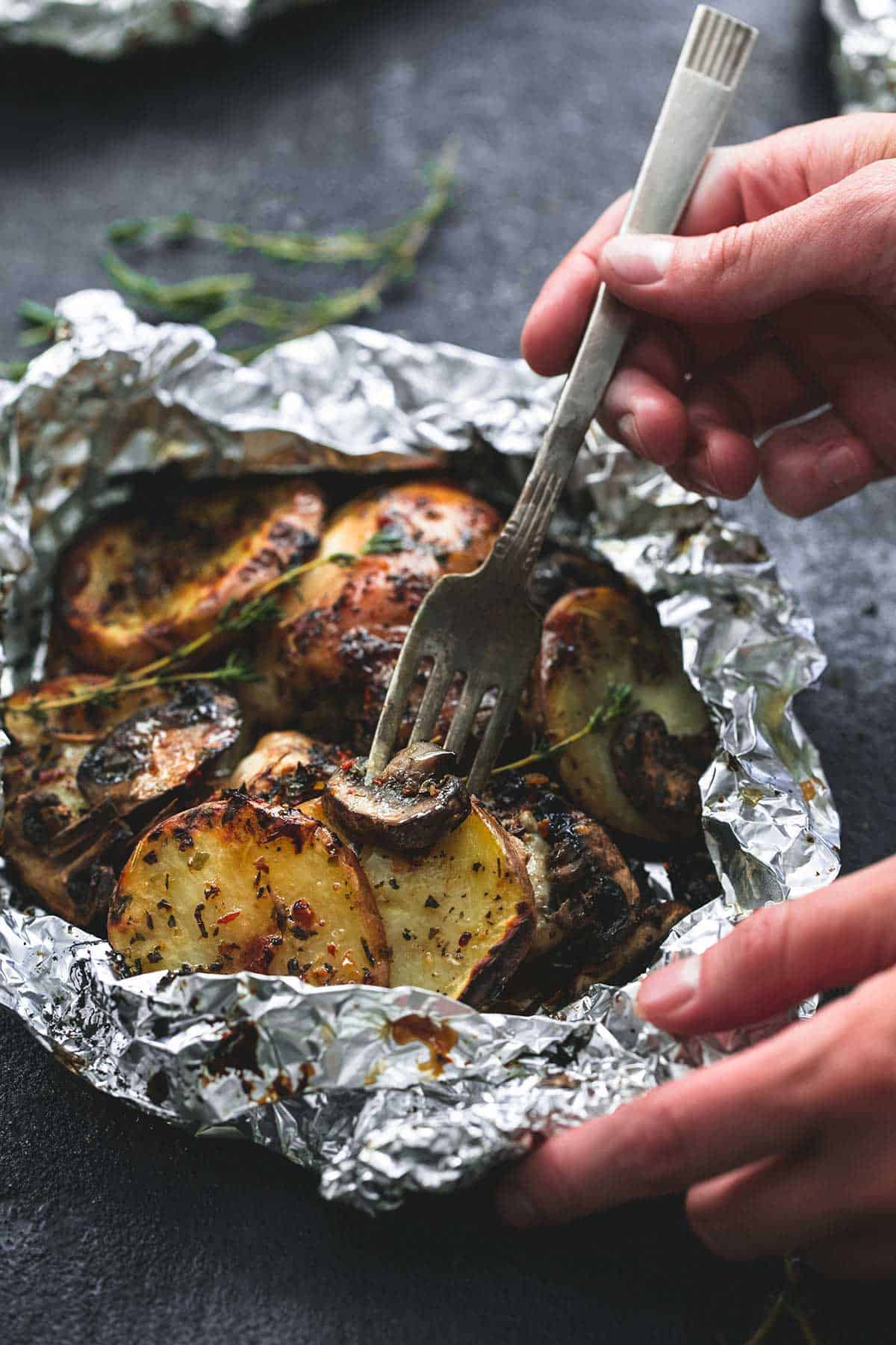 a hand grabbing a potato from a grilled herbed chicken & potato foil pack.